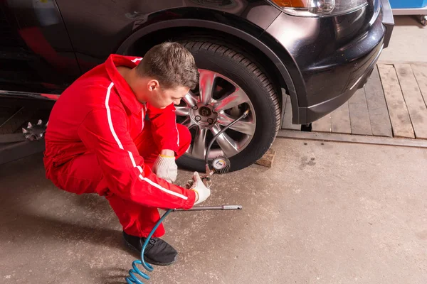 Jeune mécanicien automobile vérifiant la pression d'air d'un pneu — Photo