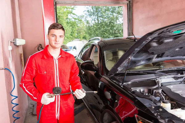 Young handsome auto mechanic holding equipment for checking the — Stock Photo, Image