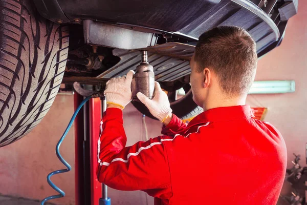 Professional male auto mechanic in uniform working underneath a — Stock Photo, Image