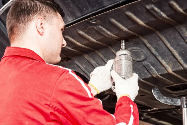 Professional young car mechanic in uniform working underneath a — Stock Photo, Image