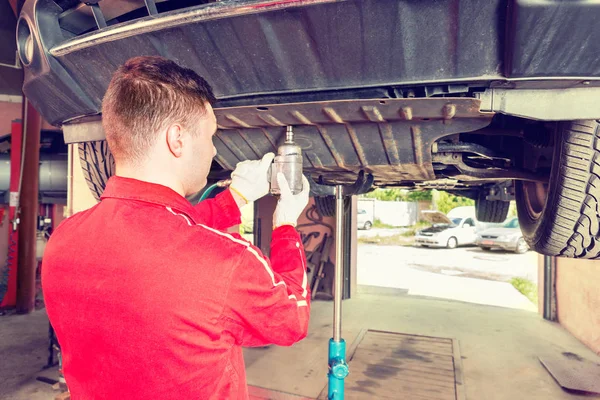 Professional young auto mechanic in uniform working underneath a — Stock Photo, Image