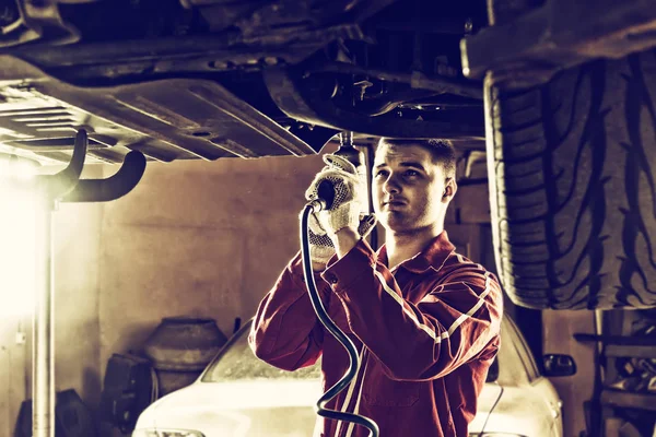 Professional handsome male auto mechanic in uniform working unde