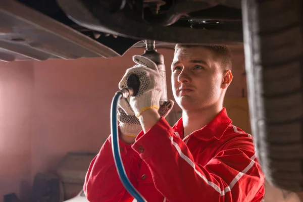 Professional handsome male car mechanic in uniform working under — Stock Photo, Image