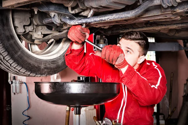 Mécanicien automobile masculin en uniforme travaillant sous une voiture relevée et — Photo