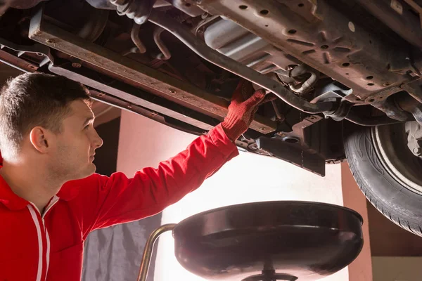 Mécanicien automobile en uniforme travaillant sous une voiture relevée et cha — Photo