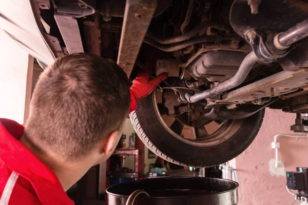 Car mechanic in uniform working underneath a lifted car — Stock Photo, Image
