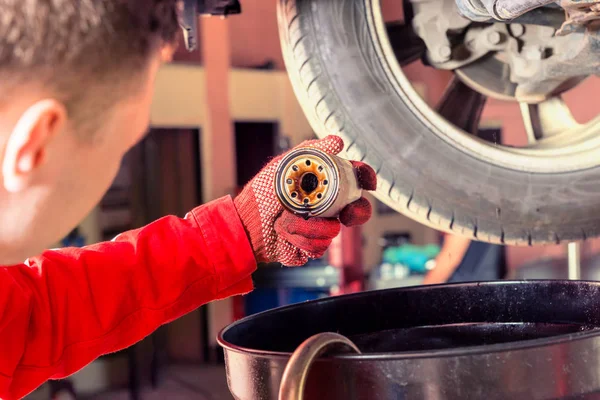 Motor mechanic in uniform working underneath a lifted car and ch — Stock Photo, Image