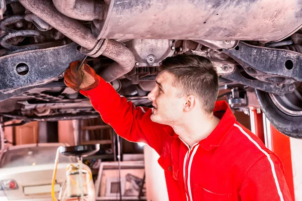 Mechanic in uniform working underneath a lifted car with working — Stock Photo, Image