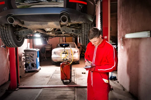 Handsome young male auto mechanic standing making notes undernea