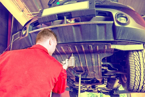 Mecânico de automóvel profissional em uniforme trabalhando sob uma elevação — Fotografia de Stock