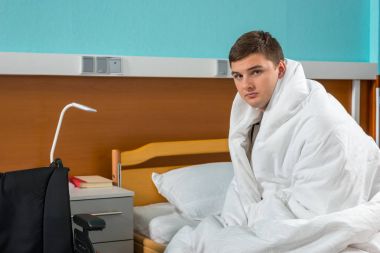 Genç erkek hasta hasta hastane yatağında oturup kaplı 