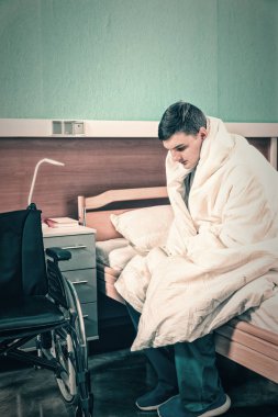 Genç üzgün erkek hasta hasta hastane yatağında oturup w kaplı