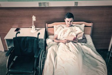 Erkek hasta hasta hastane yatağında yalan ve bir kitap okuma