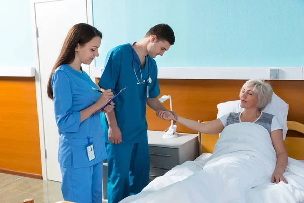 Joven médico y enfermera midiendo el pulso y los escritos — Foto de Stock