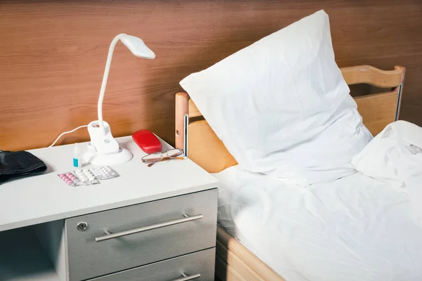 Een nachtkastje met een heleboel tabletten, een lamp en bril staat — Stockfoto