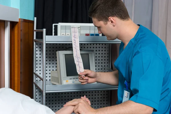 Il dottore in uniforme sta esaminando l'analisi dell'elettrocardiografo e — Foto Stock