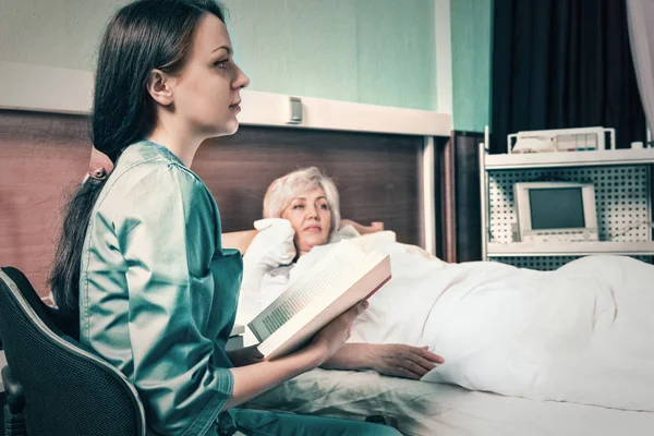 Aantrekkelijke verpleegster in uniform is het lezen van een boek voor haar patiënt — Stockfoto