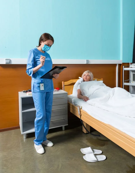 Junge Krankenschwester in Uniform mit Maske und Blick auf Klemmbrett mit — Stockfoto