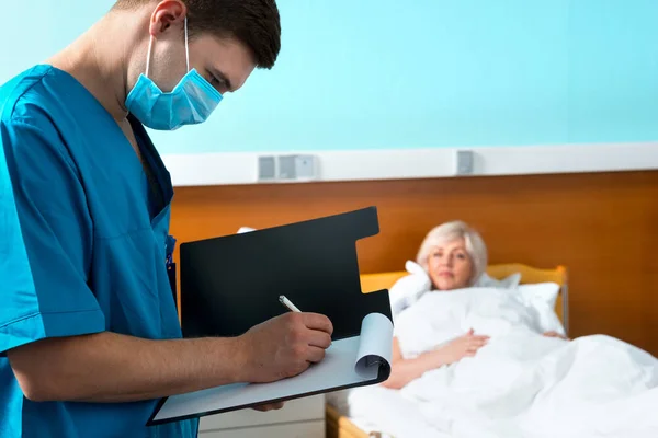 Maschio medico concentrato in uniforme indossando una maschera facendo alcuni n — Foto Stock