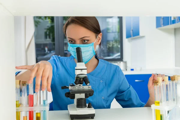 Female scientist in uniform wearing a mask is holding test tubes — Stock Photo, Image