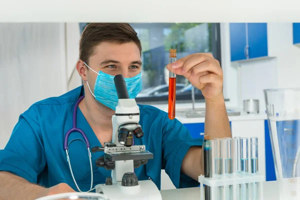 Junger männlicher Wissenschaftler in Uniform mit Maske hält Test-T — Stockfoto