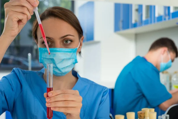 在统一戴着面具的女科学家用移液管填充 — 图库照片