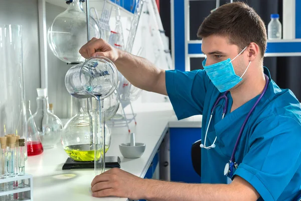 Young scientist in uniform wearing a mask is holding test glass — Stock Photo, Image