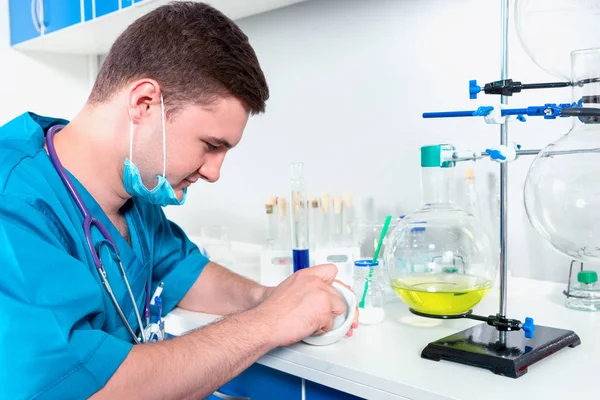 Männlicher Wissenschaftler in Uniform mit Maske, der Puder auf Cer zubereitet — Stockfoto