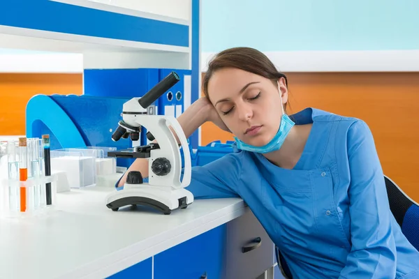Tired young female scientist in uniform is sleaping near her wor — Stock Photo, Image