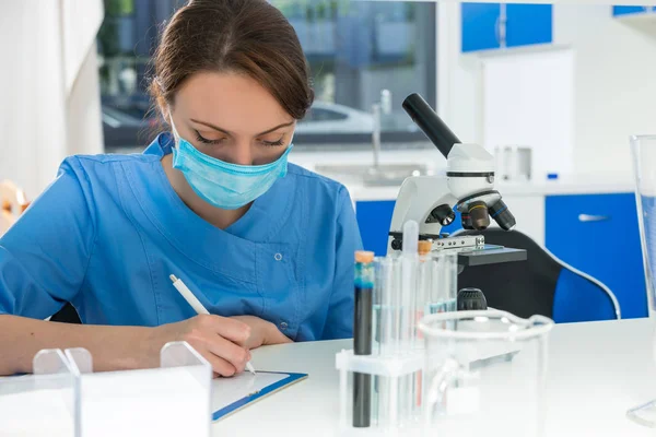 Young female scientist in uniform writing down notes of her rese — Stock Photo, Image