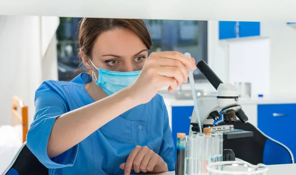 Junge Wissenschaftlerin in Uniform nimmt eine Flüssigkeit per Pipette aus — Stockfoto