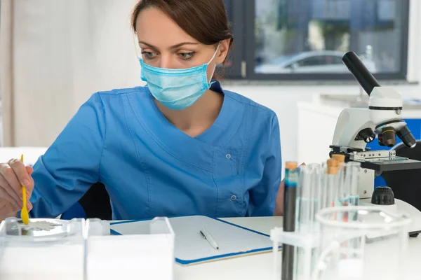 Female scientist in uniform wearing a mask weighs powder on spec — Stock Photo, Image