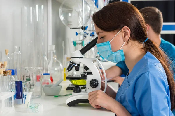 Young male and female scientists in uniform is looking through a — Stock Photo, Image