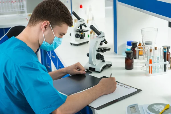 Junger männlicher Wissenschaftler in Uniform und Maske schreibt nein — Stockfoto