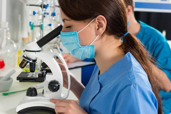 Close up of young female scientist in uniform is looking through — Stock Photo, Image