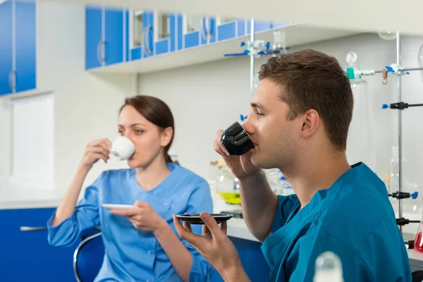 Two young scientists in uniform drinking a coffee after some res — Stock Photo, Image