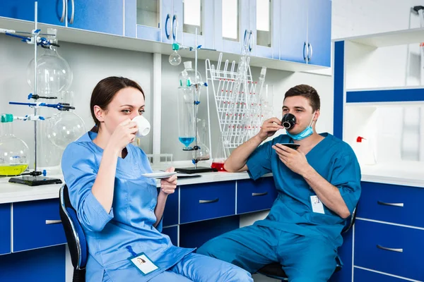 Two scientists in uniform drinking a coffee after some research — Stock Photo, Image