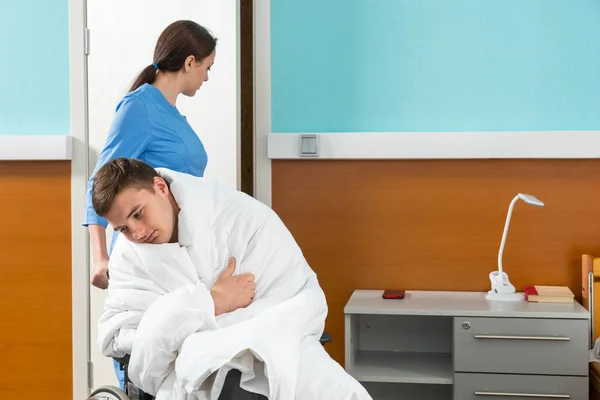 Junge Krankenschwester in Uniform zieht Rollstuhl mit kranker Patientendecke — Stockfoto