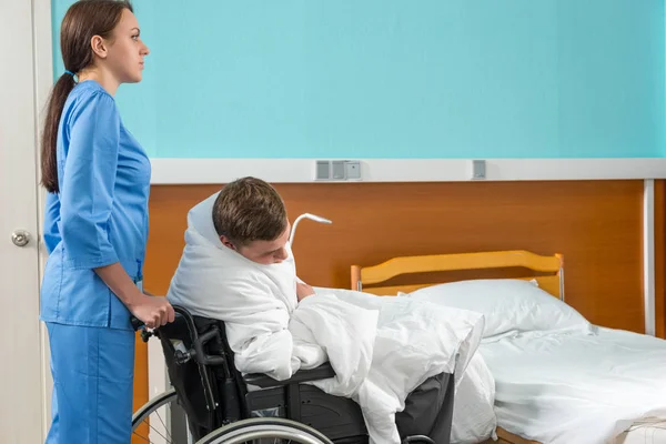 Enfermera atractiva en silla de ruedas tirando uniforme con paciente enfermo —  Fotos de Stock