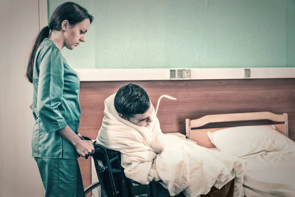Attraente giovane infermiera in uniforme tirando sedia a rotelle con pa malato — Foto Stock