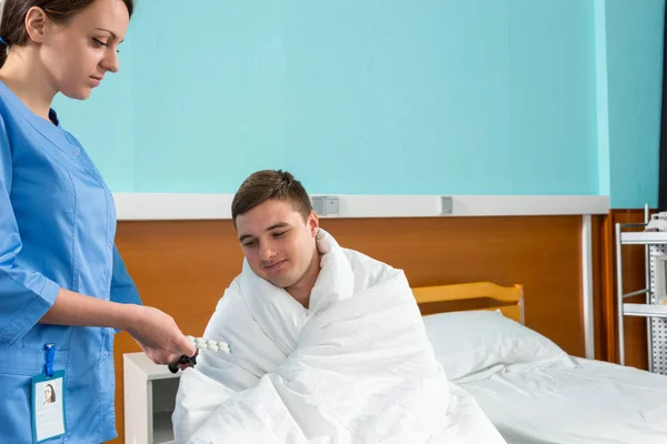 Junge attraktive Krankenschwester gibt Pillen an kranken Patienten sitzen auf wh — Stockfoto