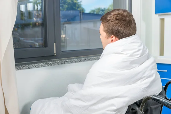 Smutny chory pacjent siedzi przez okno na wózku inwalidzkim pokryte — Zdjęcie stockowe