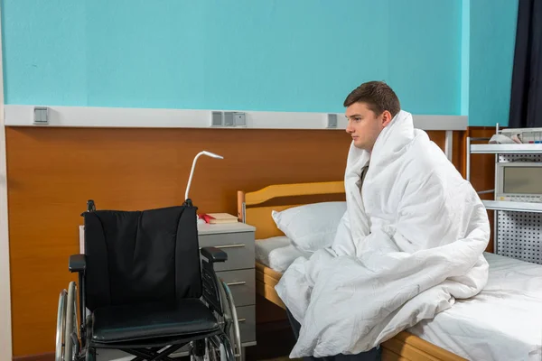 Male ill patient sitting on the hospital bed covered with quilt