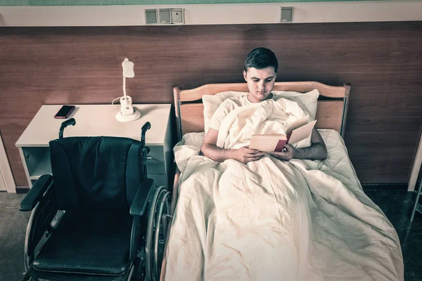 Erkek hasta hasta hastane yatağında yalan ve bir kitap okuma