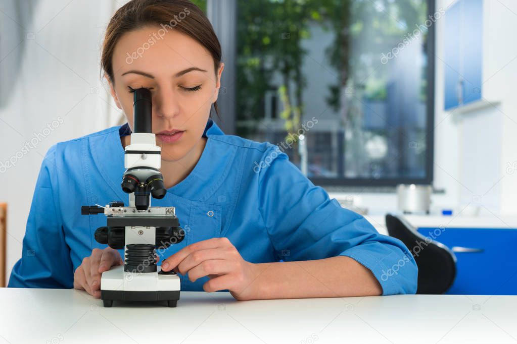 Young female scientist in uniform is looking through a microscop