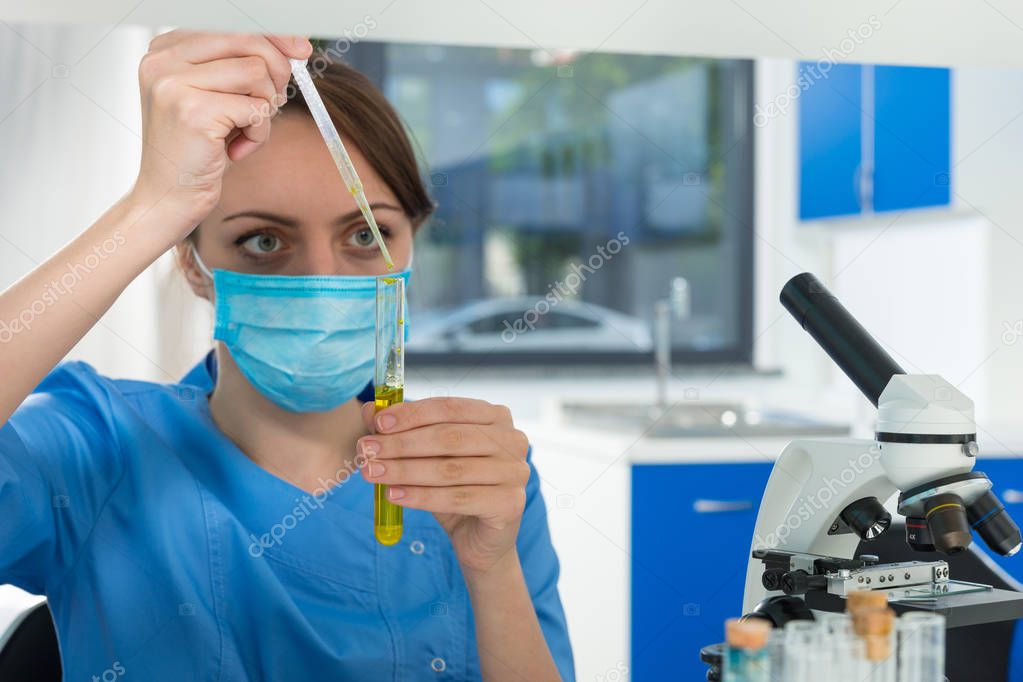 Concentrated female scientist in uniform takes a liquid by pipet