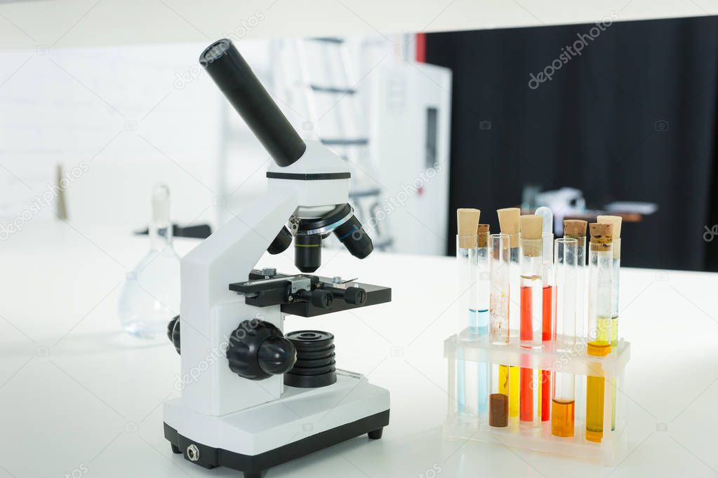 Microscope on the workplace near test tubes with different liqui