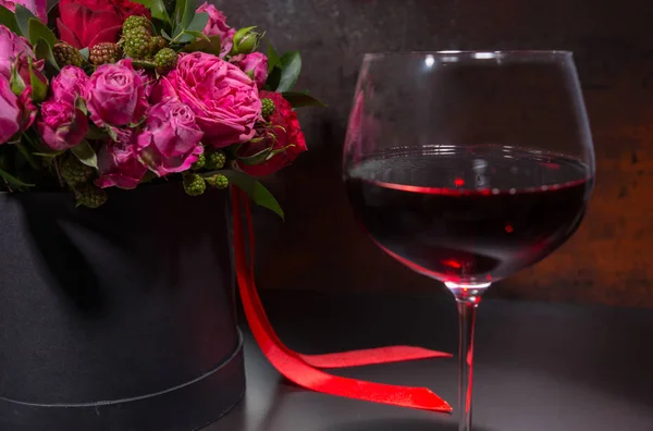 Glass with wine standing by bouquet of roses — Stock Photo, Image