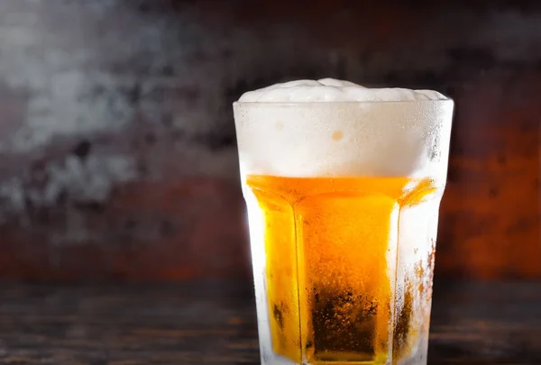 Grand verre avec une bière légère et une tête de mousse sur un vieux bureau sombre — Photo