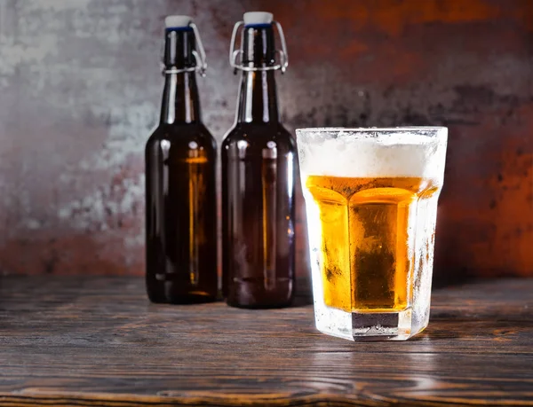 Two beer bottles next to glass with a light beer and a head of f — Stock Photo, Image